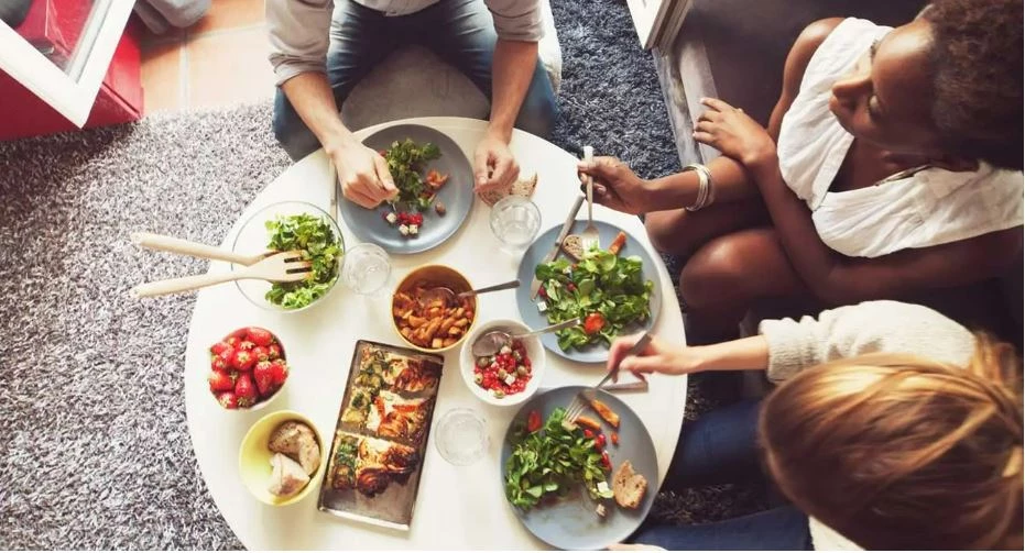 Flera personer äter hälsosam mat med mycket grönsaker runt ett bord